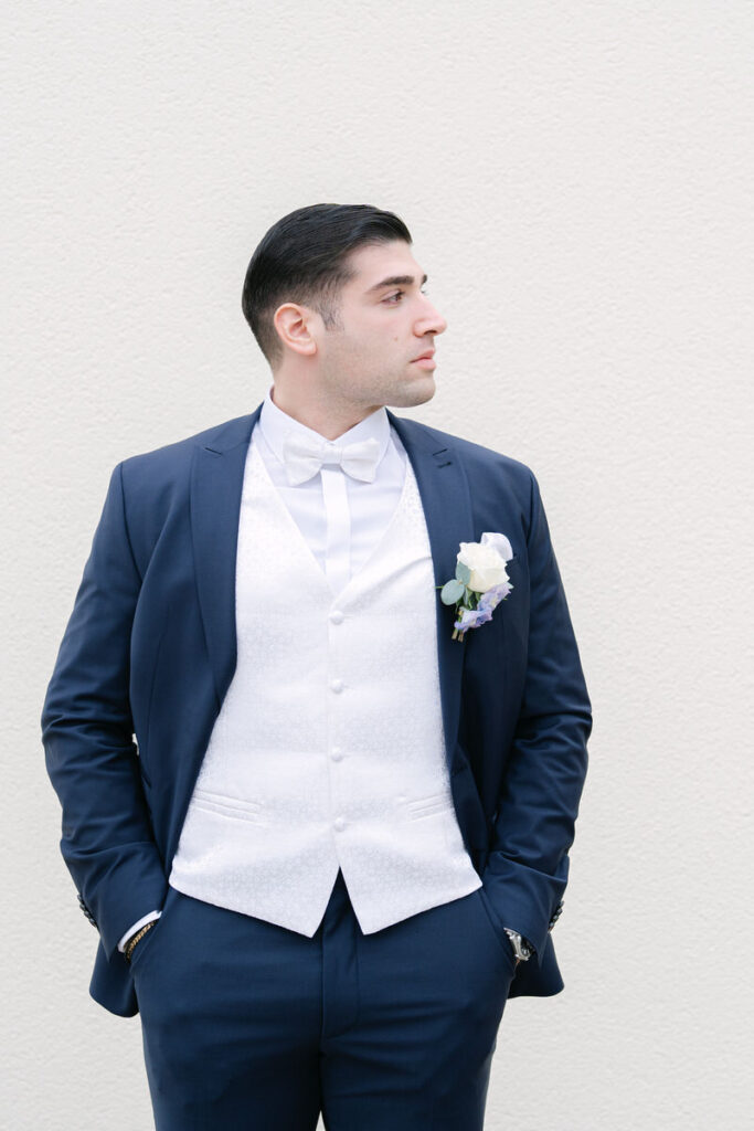 Bräutigam mit einem blauen Hochzeitsanzug und einem weißen Anstecker vor einem hellen Hintergrund