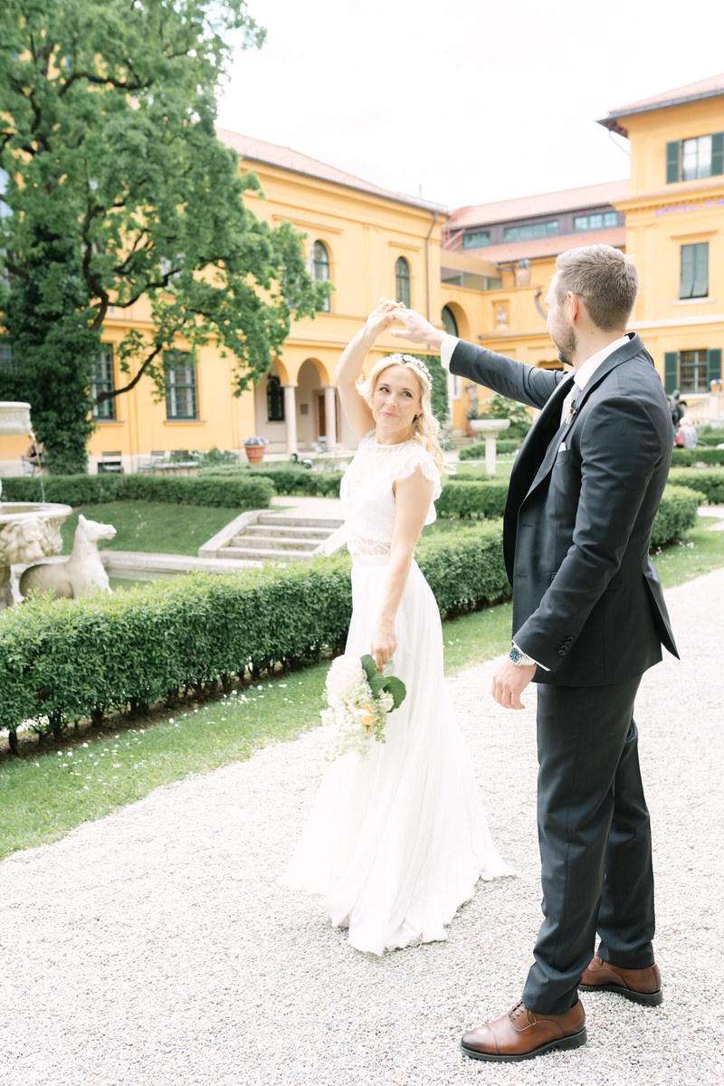 Braut dreht sich an der Hand des Bräutigams und lächelt ihn an, während sie einen Hochzeitsstrauß hält