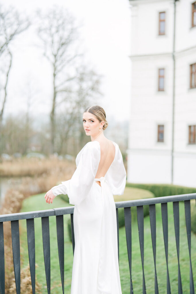 Braut blickt zum Hochzeitsfotografen Rosenheim und präsentiert einen tiefen Rückenausschnitt