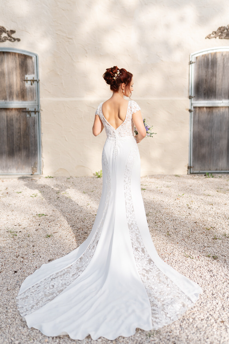 Rückenansicht eines Brautkleides mit Spitze und langer Schleppe mit einer hellen Wand im Hintergrund