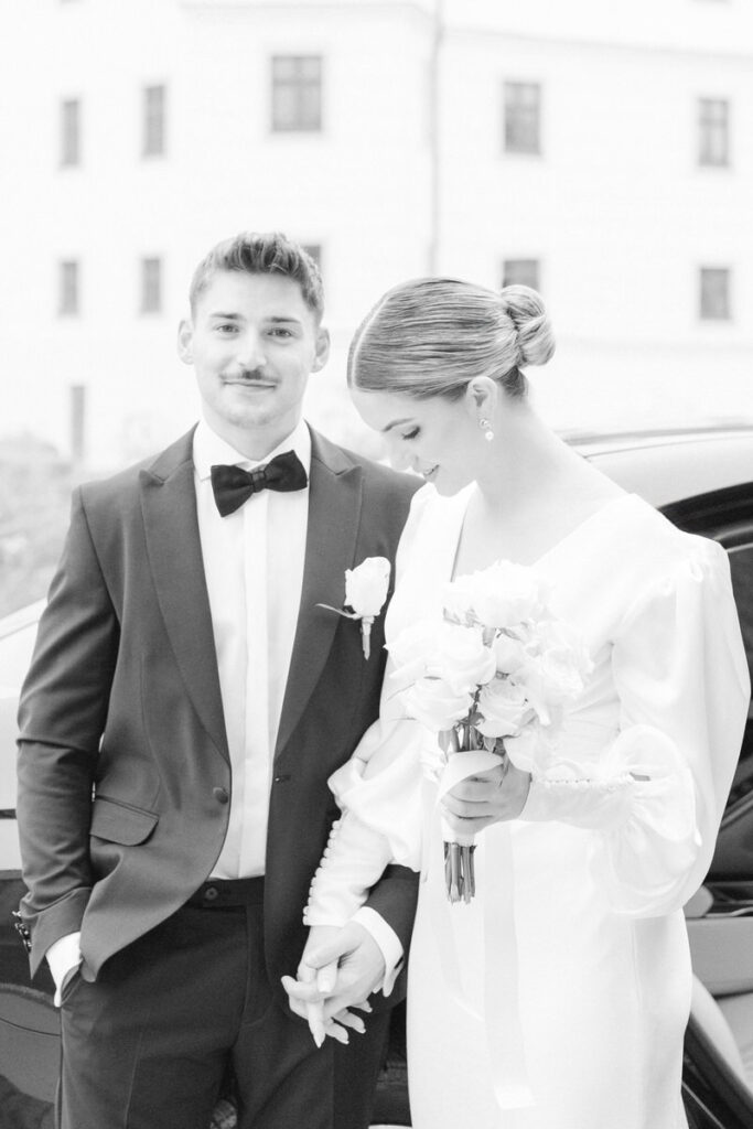 Brautpaar hält Hände vor einer Schlosskulisse, der Bräutigam lächelt beim Hochzeitsshootign mit dem Hochzeitsfotografen