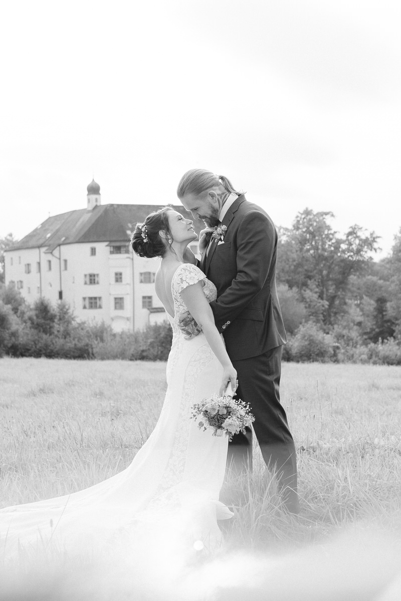 Brautpaar lächelt sich vor ihrer Hochzeitslocation in Amerang bei Rosenheim während einem Brautpaarshooting an, fotografiert in schwarz weiß