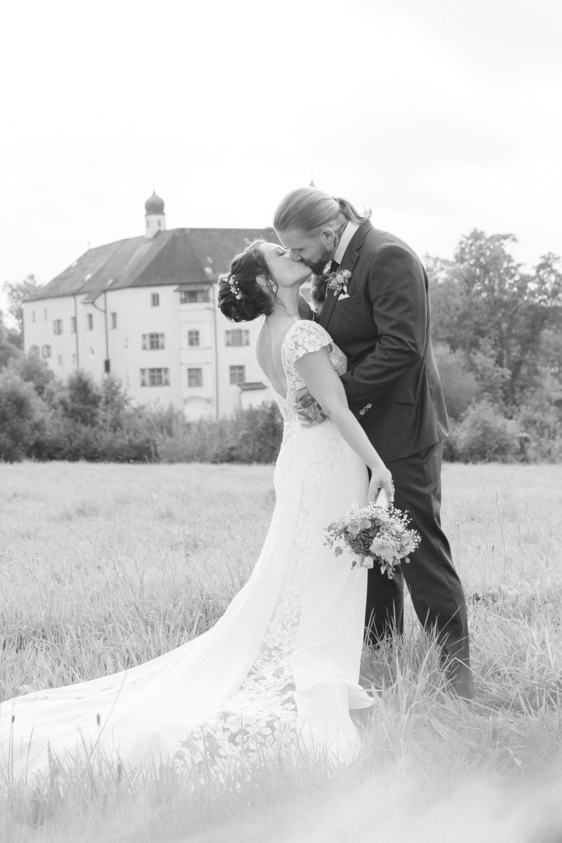 Verliebtes Hochzeitspaar küsst sich mit Hochzeitslocation in der Nähe von Rosenheim beim Brautpaarshooting mit dem Hochzeitsfotografen Rosenheim