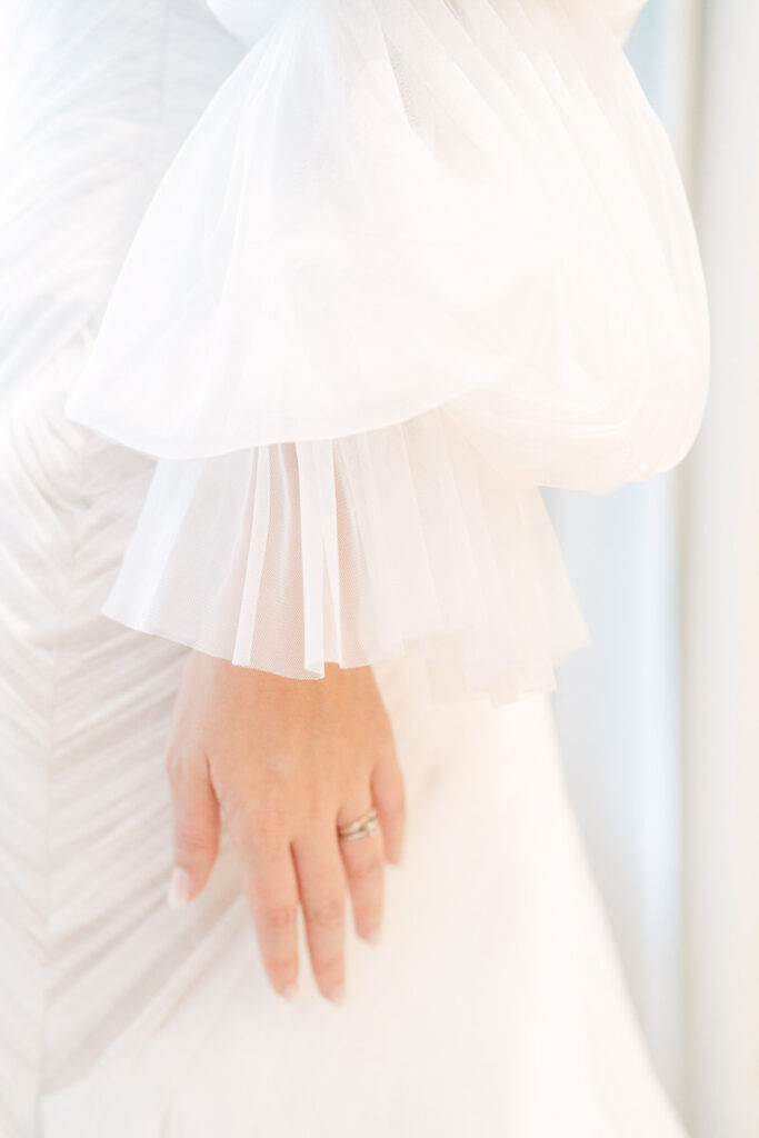 Nahaufnahme von einem eleganten Brautoutfit mit Tüll und einem Ehering an der Hand
