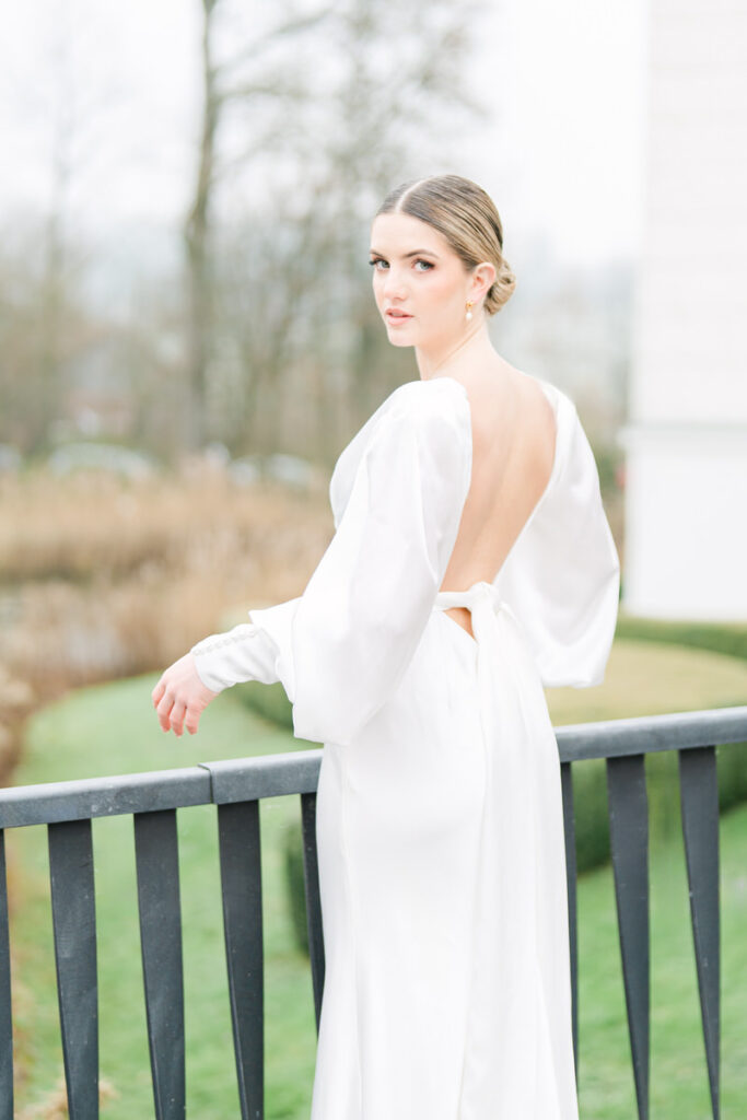 Braut mit tiefem Rückenausschnitt blickt zum Hochzeitfotograf Rosenheim während dem Hochzeitsshooting
