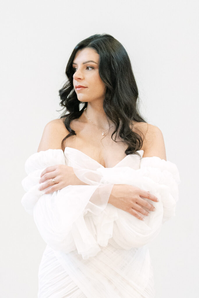 Braut sieht auf die Seite und verschränkt ihre Arme im modernen Brautkleid aus Tüll beim Brautshooting