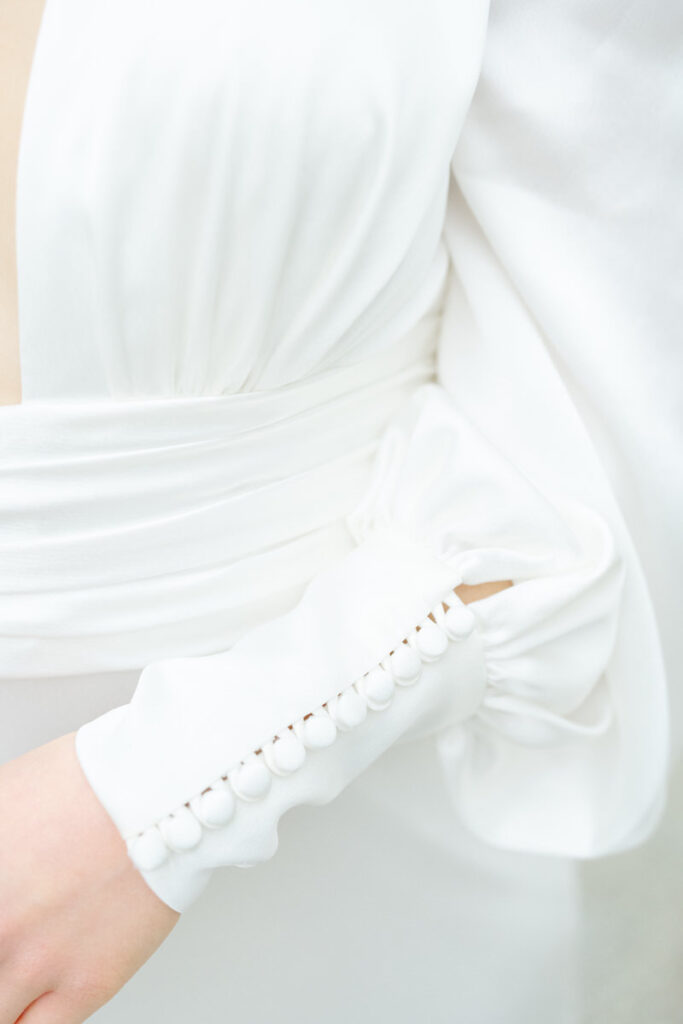 Detailfoto von einem Hochzeitsoutfit aus Satin mit einer eleganten Knopfleiste am Ärmel des Brautkleides