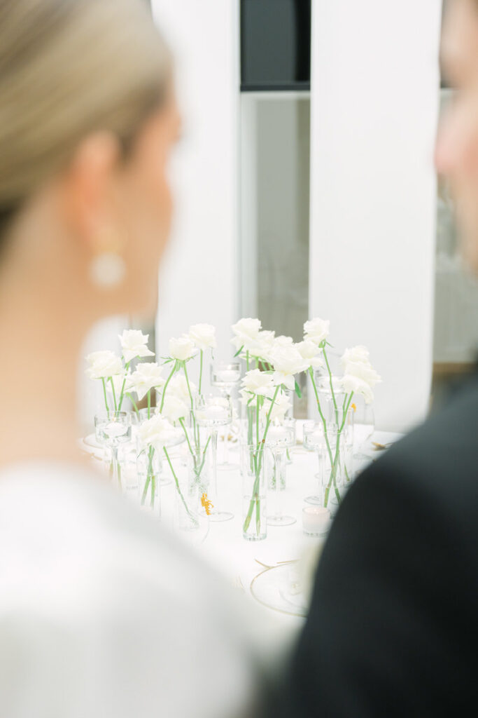 Detailaufnahme vor einem runden Hochzeitstisch mit weißen Blumen und goldenen Akzenten während das Brautpaar auf den Tisch blickt