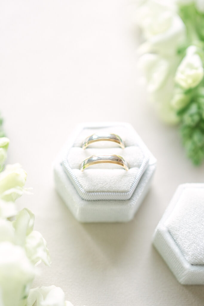 Detailaufnahme von goldenen Hochzeitsringen in einer weißen Ringschachteln von weißen Blumen umgeben