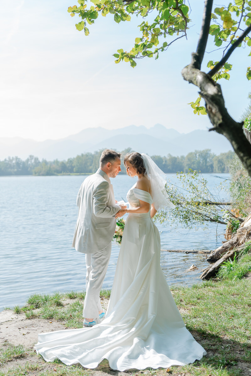 Brautpaar hält sich am Happiger See in Rosenheim die Hände während ihrem emotionalen first Look mit Bergblick