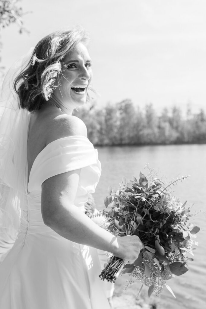 Eine Braut lacht in die Kamera beim first Look am Happiger See, schwarz weiß Bild von Hochzeitsfotograf Rosenheim