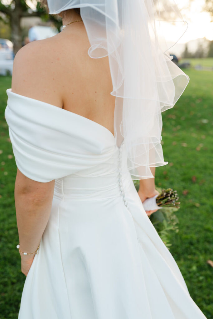Ausschnitt von einem Brautkleid, die Braut hält einen Blumenstrauß in der Hand.