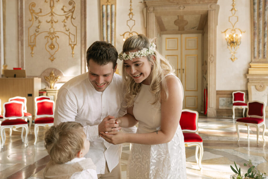Braut und Bräutigam halten Hände und lachen mit ihrem Kind im Standesamt Salzburg
