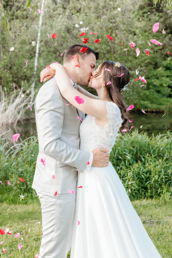 Brautpaar küsst sich beim Hochzeitsshooting mit herabregnenden Rosenblüten